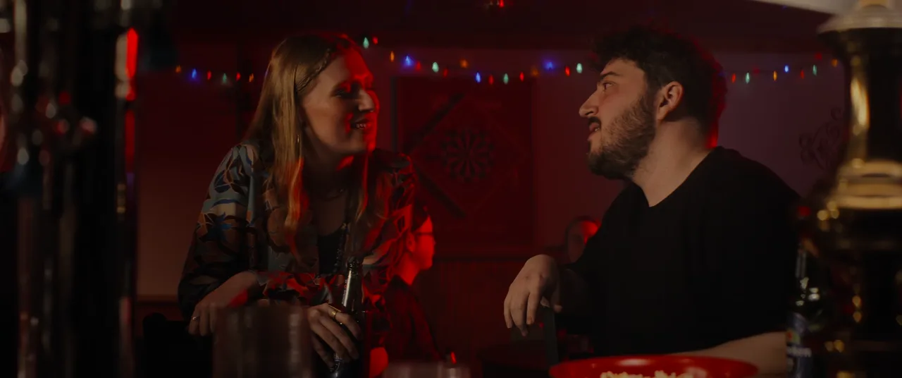 Still from It's Always Almost Over — Ricky DeRosa in a red-lit bar scene